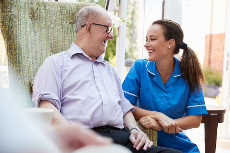 A caregiver assisting an elderly man in a chair