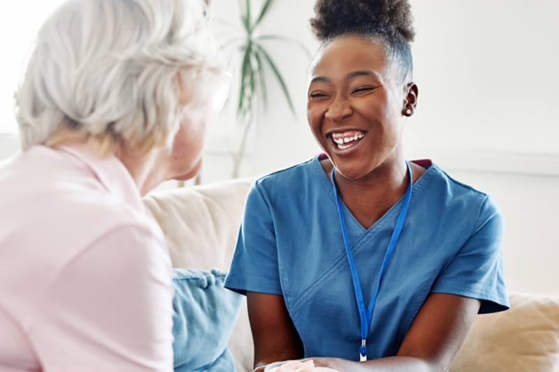 A smiling female nurse listens attentively to an elderly woman during a friendly conversation